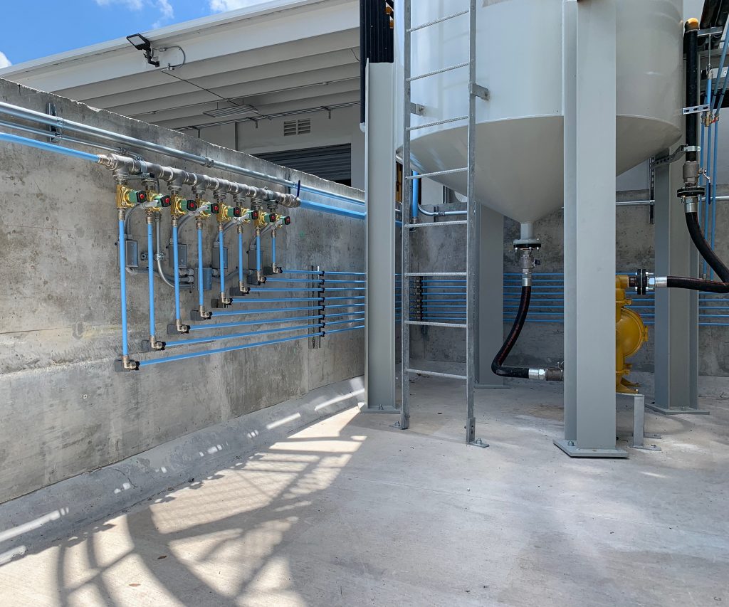 Industrial setting showcasing Arle Compressors of Florida, pipework and valves connected to large storage tanks with shadows casting over a concrete floor on a sunny day.